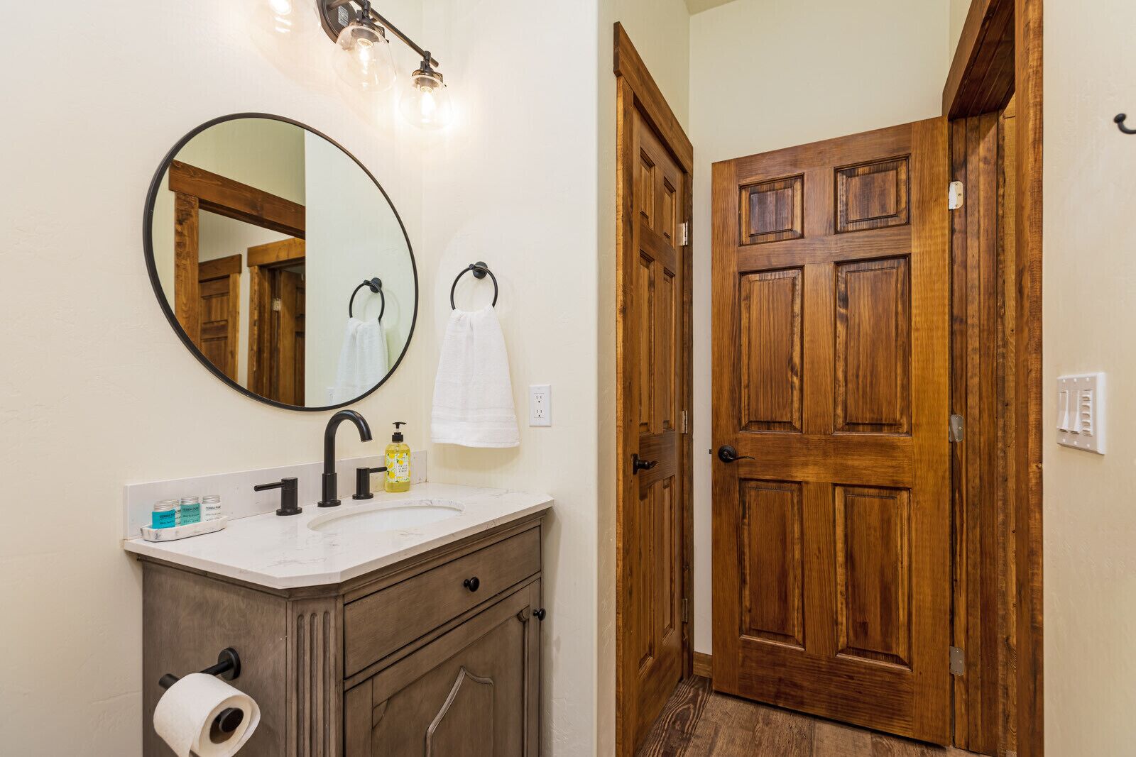 A bathroom with a round mirror, a sink with toiletries, and a wooden door.