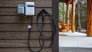 Sähköauton latausasema on asennettu puiseen seinään, ja sen edessä on betonilattia sekä ulkona oleva oleskelualue.