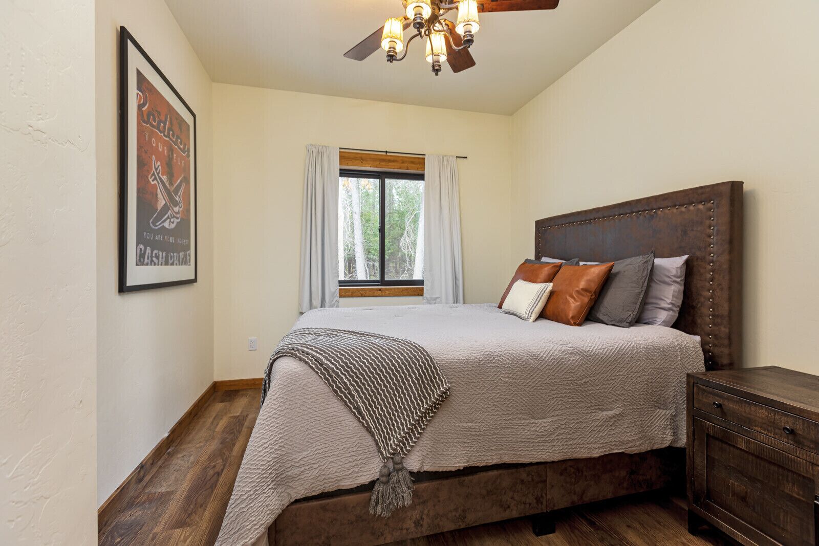 A bedroom with a large bed, a wooden headboard, a nightstand, and a window with curtains.