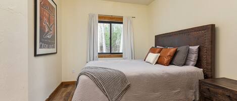 Ein Schlafzimmer mit einem großen Bett, einem Holzkopfende, einem Nachttisch und einem Fenster mit Vorhängen.