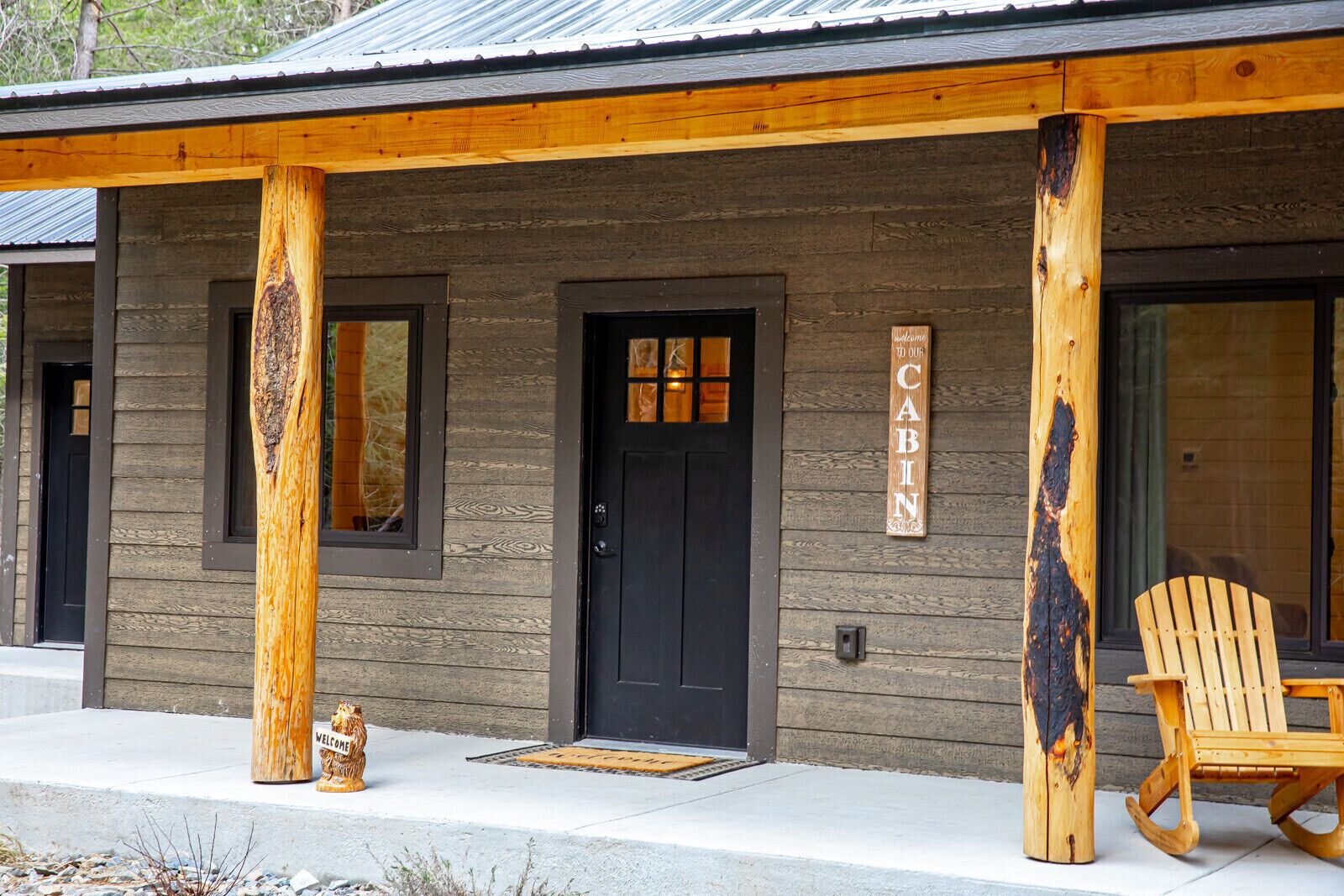 Un bâtiment de style cabane avec une porte noire, une pancarte d’accueil et une inscription « CABANE » sur le mur.