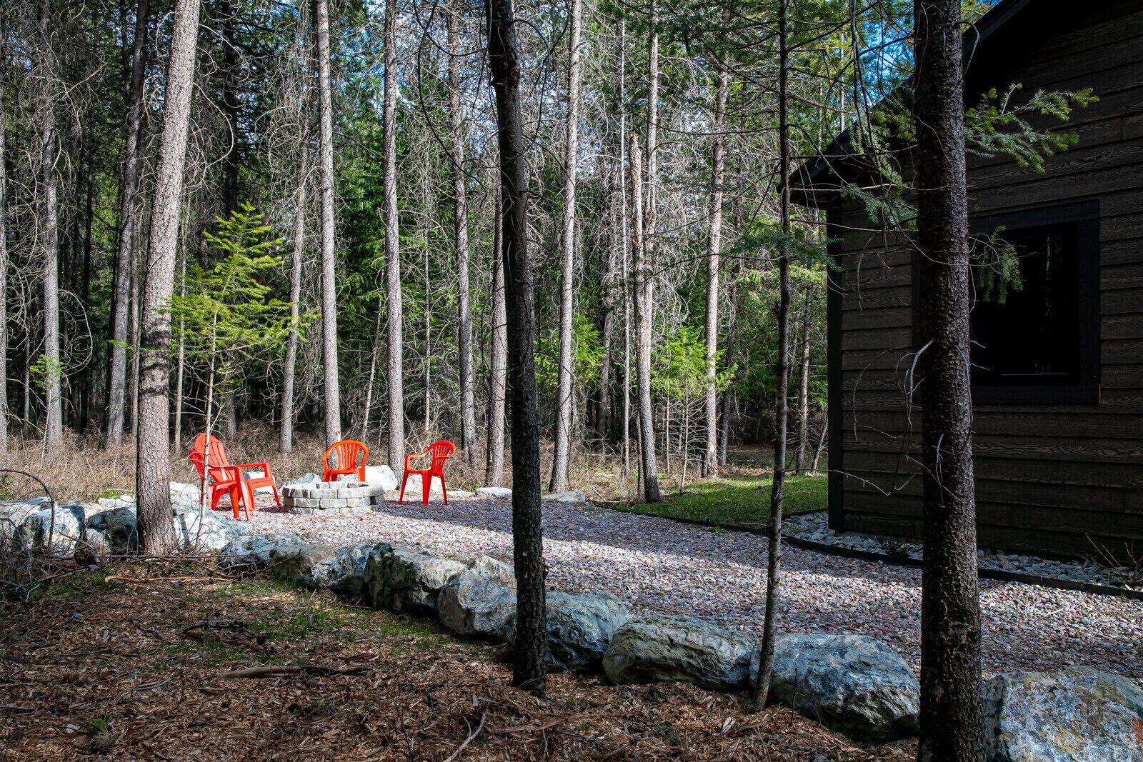 A cabin with a gravel path leading to a seating area with three red chairs.