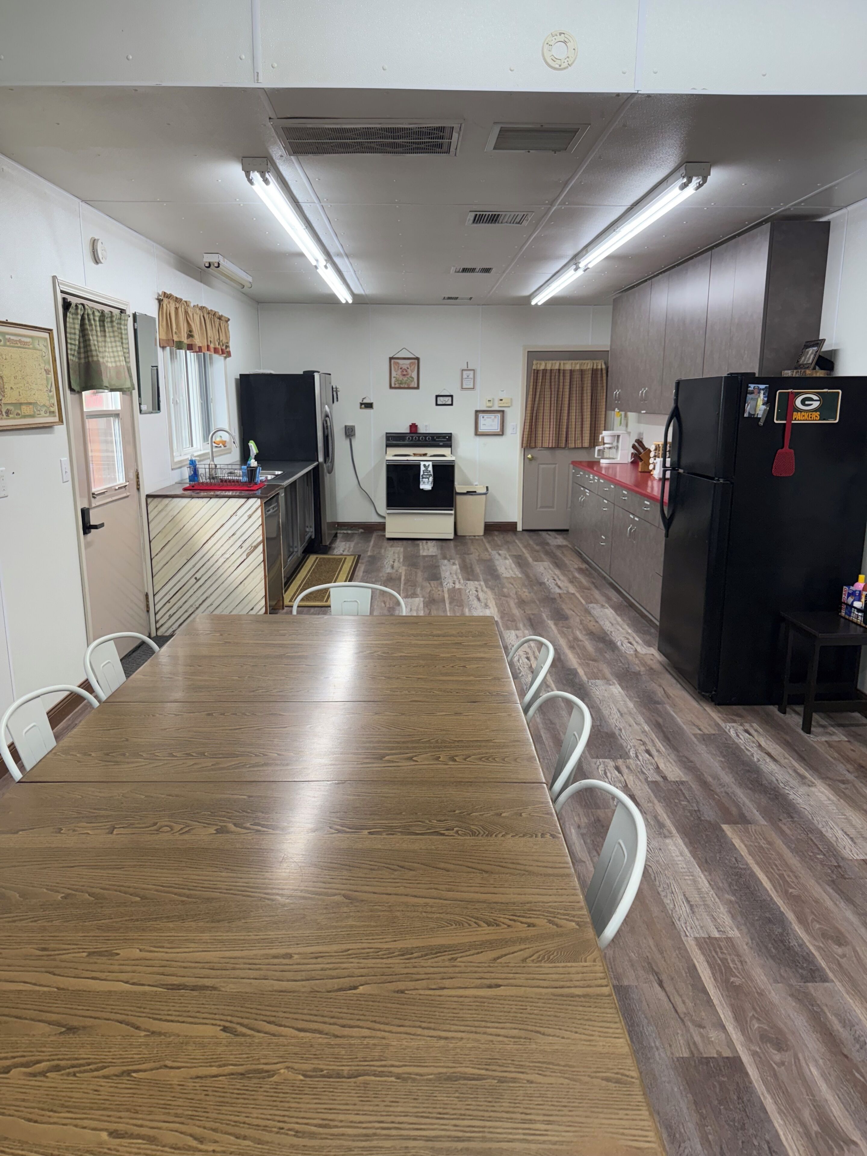 A kitchen with a wooden dining table, white chairs, a refrigerator, and a stove.