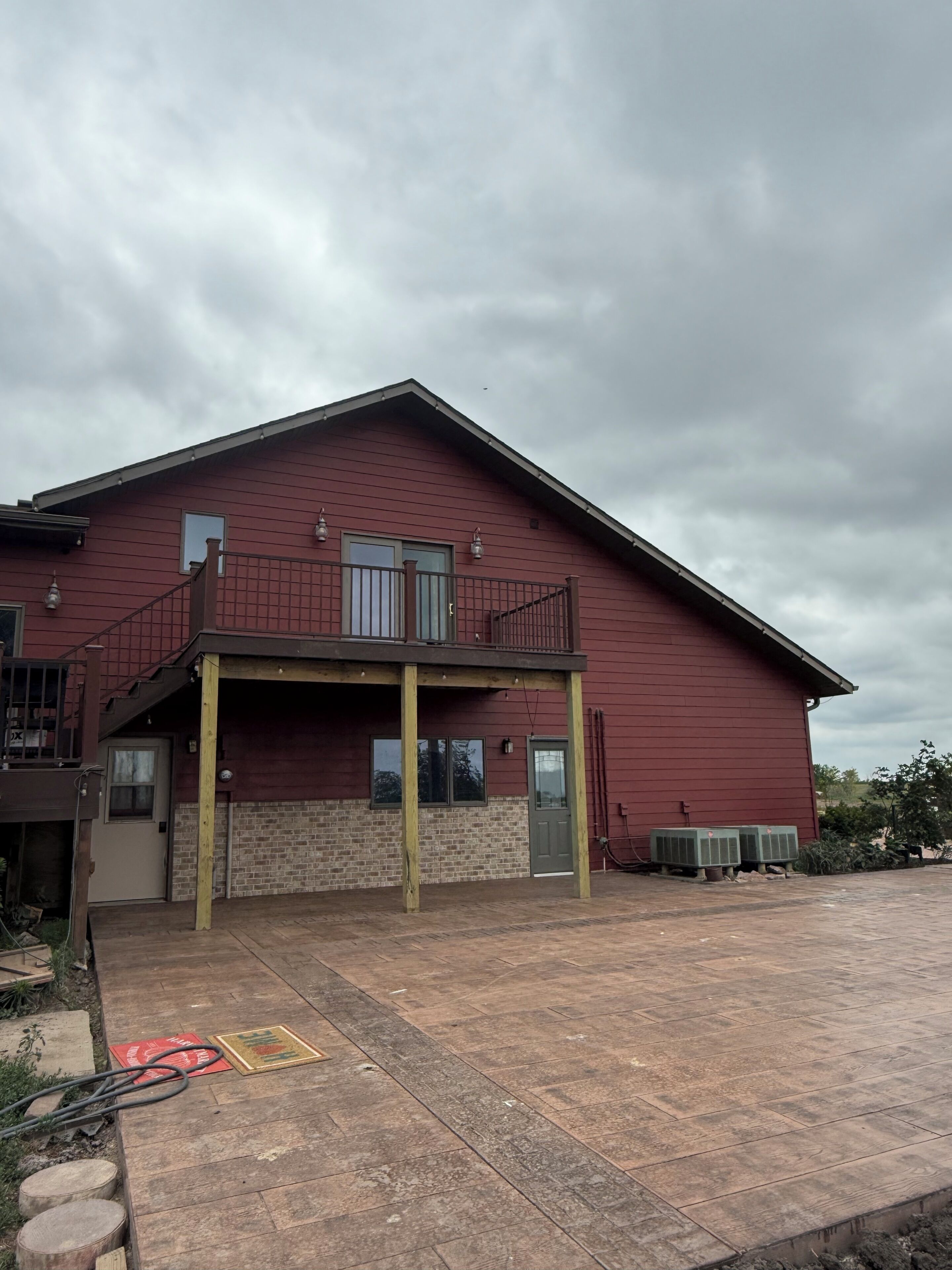 A red building with a balcony, a covered porch, and a paved entrance area.