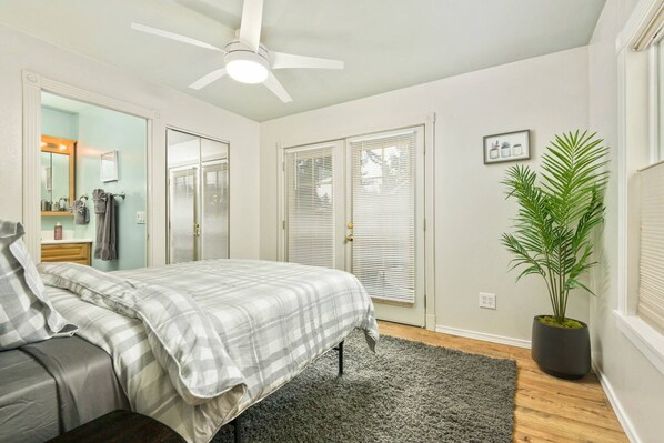 A bedroom with a bed, a ceiling fan, a potted plant, and a window with blinds.