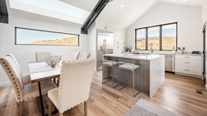 A modern kitchen with a large island, bar stools, and a view of a desert landscape through large windows. - Luxury in Old Town, Walk to Main St. and Town Lift, Forever Views!

 (Park City)
