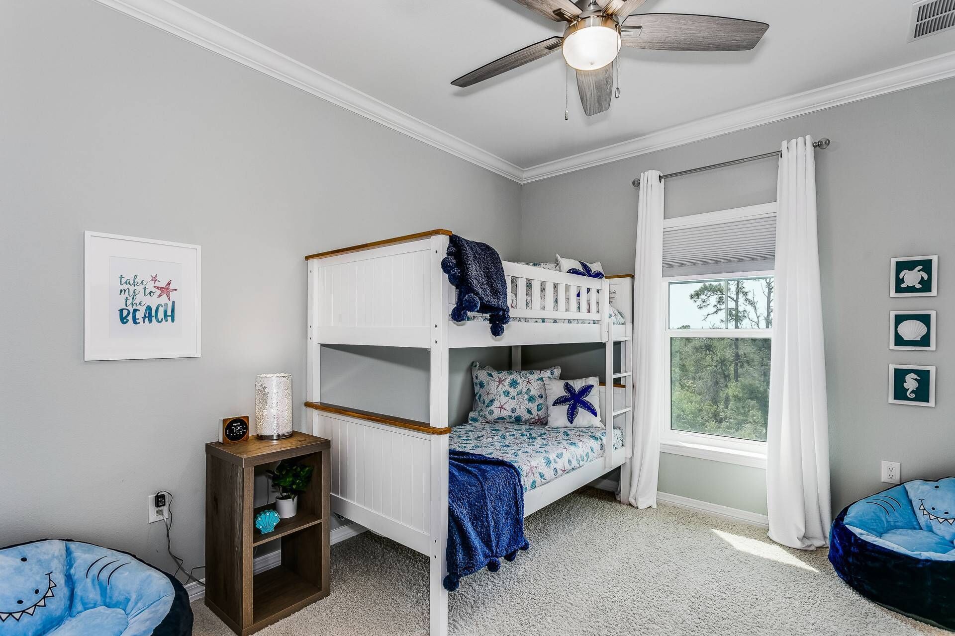 Ein Kinderstockbett mit Deckenventilator, einem fenster mit Vorhängen und Strandbilder an der Wand.