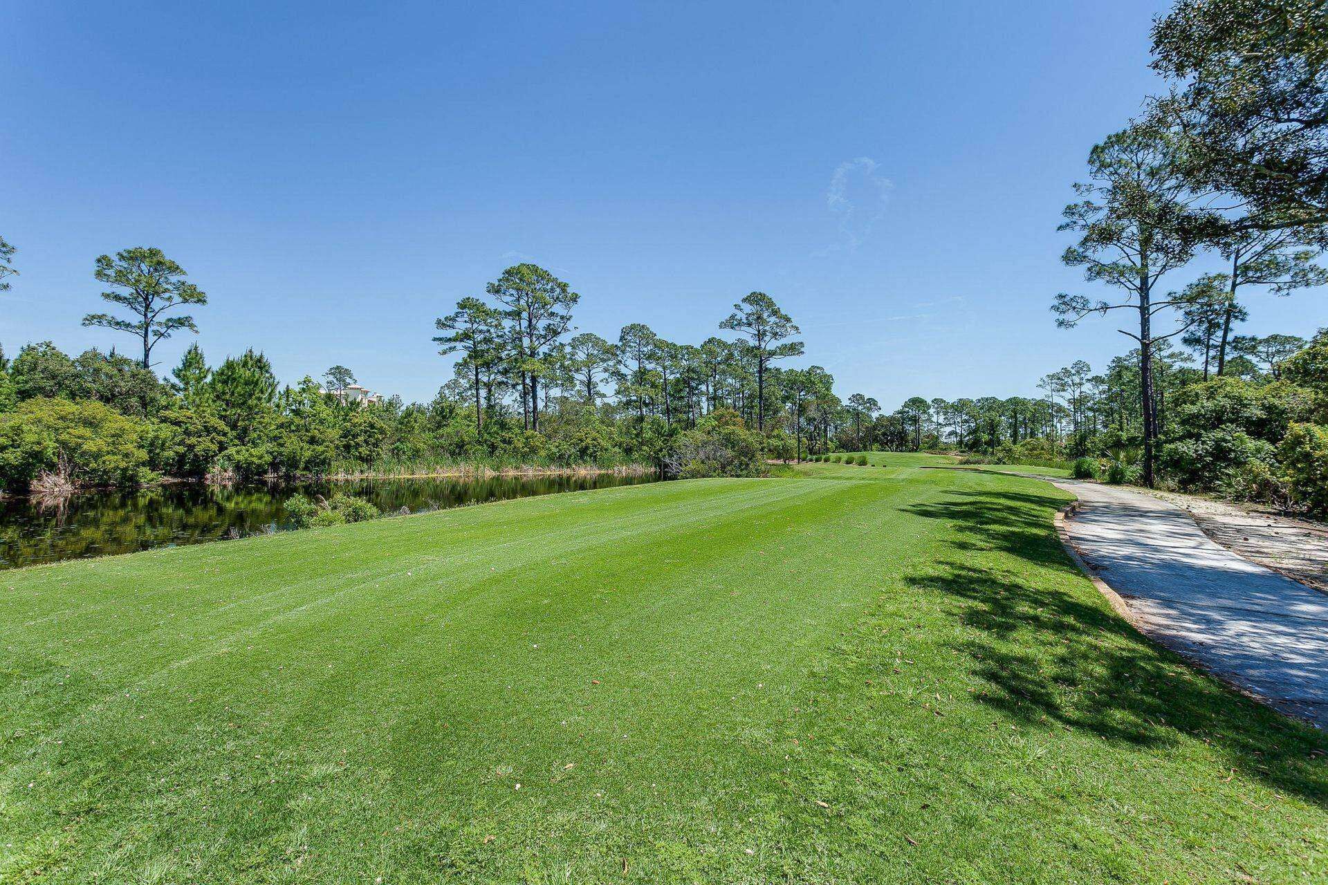 A well-maintained grassy area with a pathway leading to a body of water, surrounded by trees and vegetation.