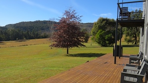 Um deck de madeira com mobiliário para área externa, uma árvore e vista para uma paisagem montanhosa.