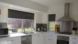 Cozinha moderna com armários brancos, eletrodomésticos de aço inoxidável e uma grande janela com vista para árvores.