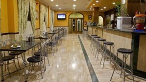 A hotel dining area with long tables and bar stools, a television screen, and a coffee machine. - Los Dolmenes (Antequera)
