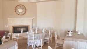 A dining area with round tables and white chairs, a fireplace, and a clock on the wall. - Los Dolmenes (Antequera)
