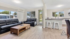 Un salon moderne avec un canapé en cuir noir, une table basse en bois et un espace cuisine blanc doté d’un comptoir-bar.