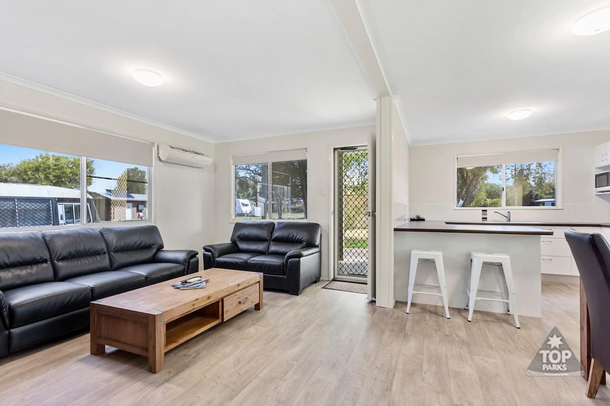 Una sala de estar moderna con un sofá de cuero negro, una mesa de centro de madera y una cocina blanca con barra.