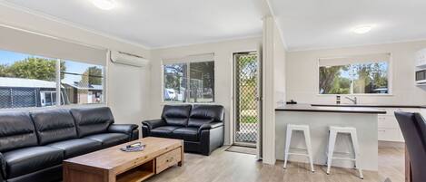 Una sala de estar moderna con un sofá de cuero negro, una mesa de centro de madera y una cocina blanca con barra.