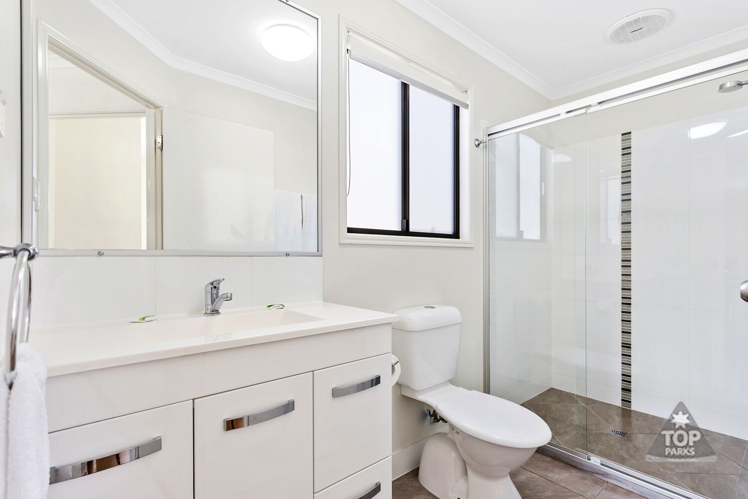 Un baño moderno con tocador blanco, un espejo grande, un inodoro y una cabina de ducha con mampara de vidrio.