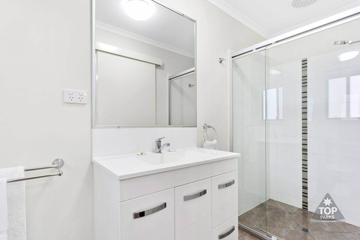 Un baño moderno con tocador blanco, un espejo grande y un box de ducha de vidrio.