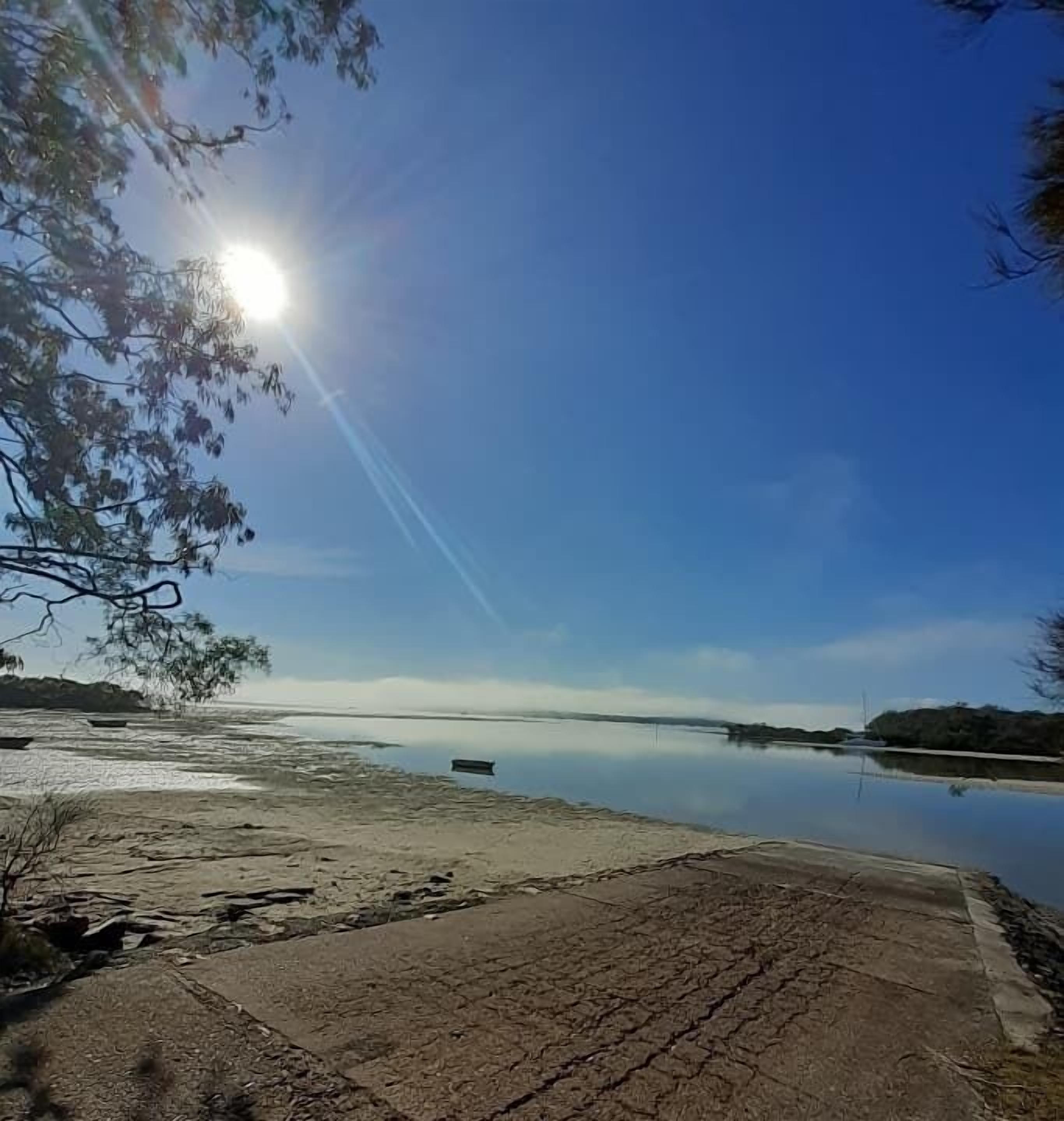 Un lago tranquilo con cielo despejado y reflejos de luz solar en el agua.