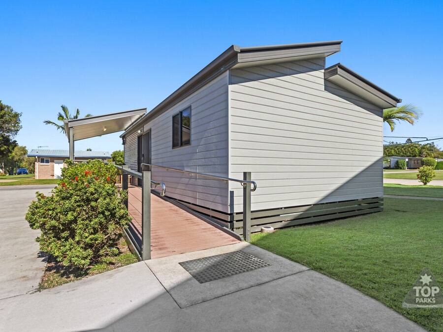 A single-story mobile home with a covered porch, a small front yard, and a clear blue sky.