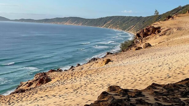 Un paysage côtier caractérisé par une plage de sable, des affleurements rocheux et une vue dégagée sur l’océan.