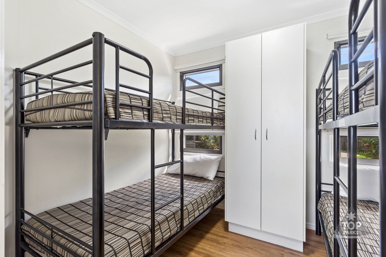 Une chambre avec un lit superposé, une fenêtre, des murs blancs et une armoire.