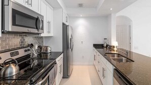 A modern kitchen with stainless steel appliances, a granite countertop, and white cabinetry.