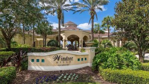 The exterior of Windsor Hills Clubhouse with a central archway, surrounded by lush greenery and palm trees.