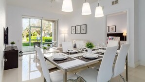 A modern dining area with a large table set for four, white chairs, and pendant lighting.
