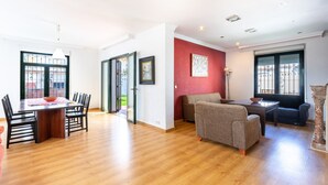 A spacious living area with a wooden floor, a dining table with chairs, a sofa, and a window with decorative iron bars. - Air-Conditioned Villa "Mascota Rincón de la Victoria" with Pool, Garden & Wi-Fi (Rincón de la Victoria)