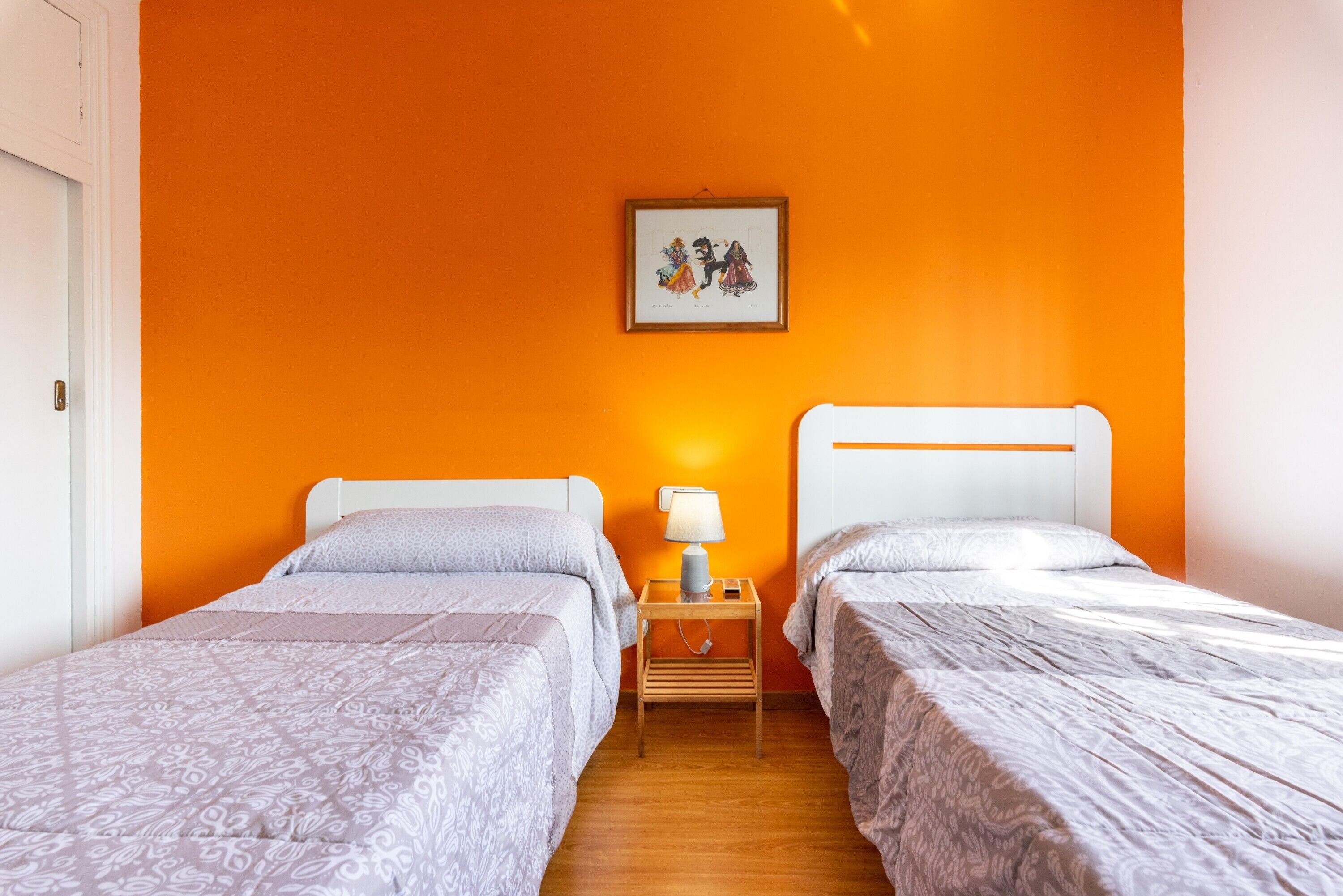 Une chambre avec deux lits, une table de chevet avec une lampe et un tableau encadré au mur.