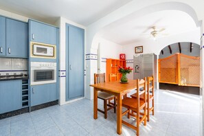 Une cuisine avec des armoires bleues, une table à manger en bois et un ventilateur de plafond.