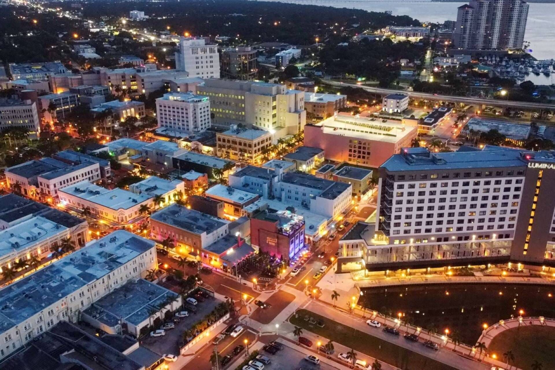 A cityscape at dusk with illuminated buildings, a prominent hotel named 'LUMINA', and a waterfront area.