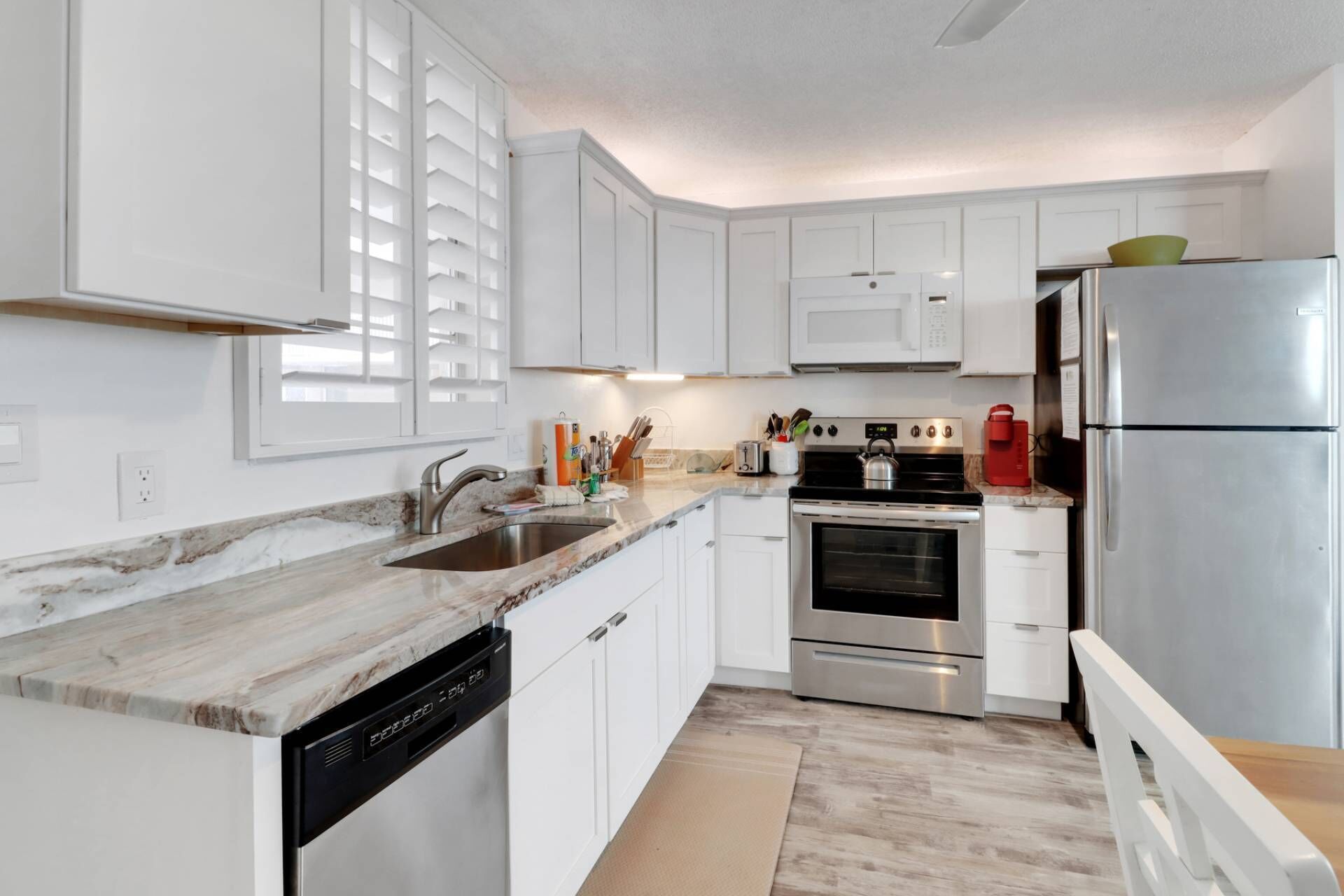 A modern kitchen with white cabinets, a stainless steel refrigerator, a built-in oven, and a dishwasher.