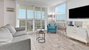 Un salon moderne avec un canapé gris, un fauteuil turquoise, une table basse ronde et un téléviseur à écran plat fixé au mur.