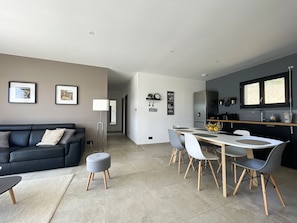 A modern living room with a black sofa, a round ottoman, and a dining area with a white table and grey chairs. - 4* villa with 2 bedrooms, air conditioning and private pool (Vagnas)