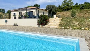 Et hus med swimmingpool, terrasse og en statue.