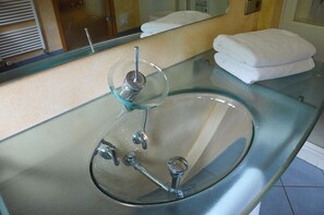 Een badkamer met een glazen wastafel, een spiegel en een stapel handdoeken.