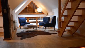 A cozy room with a sloped ceiling, wooden staircase, and a large window. There are two blue chairs, a small table, and a lamp. - Fewo 7 - Hauptmann (Todtnau)