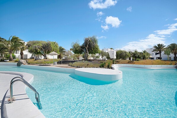 A swimming pool with a curved edge, surrounded by palm trees and buildings.