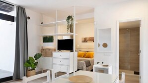 A modern, well-lit room with a glass dining table, white furniture, a TV on a white stand, and a bed with yellow pillows. - Studio Calimar Los Molinos with Pool, Wi-Fi & Terrace (Costa Teguise)