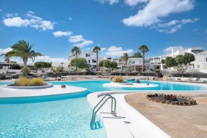 A swimming pool with a palm tree, lounge chairs, and white buildings in the background.
