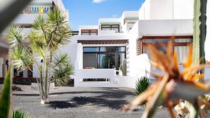 A modern building with a flat roof, large windows, and a courtyard with plants. - Studio Calimar Los Molinos with Pool, Wi-Fi & Terrace (Costa Teguise)
