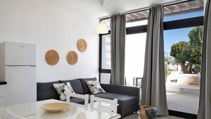A modern living room with a sofa, a glass table, and a view of the outdoors. - Studio Calimar Los Molinos with Pool, Wi-Fi & Terrace (Costa Teguise)