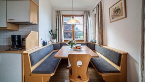 A dining area with a wooden table and bench seating, a coffee machine, and a window with curtains.