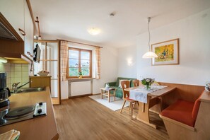 A compact kitchen with a dining area, a window with a view, and a painting on the wall. - Apartment "Hahnenkamm Rainegg" with Mountain View, Wi-Fi, Garden & Balcony (Schenna)