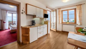 Une cuisine compacte avec des meubles blancs, un plan de travail en bois, une cuisinière intégrée et une fenêtre avec des rideaux.