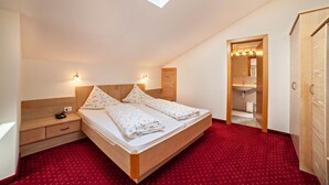 Ein Schlafzimmer mit Dachfenster, einem hölzernen Bett, einem Nachttisch, einem roten Teppich und einem durchgehenden Gang sichtbaren Badezimmer.