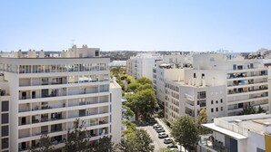A multi-story residential building with balconies, a parking area, and trees in the foreground.