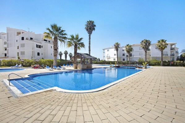 A swimming pool with a sunshade structure, lounge chairs, and palm trees.
