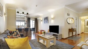 A living room with a sofa, coffee table, TV, and a dining area with chairs and a table. - Estrela do Vau Apartment with Sea View, Pool, A/C, Wi-Fi, Garden, Terrace and Balcony (Portimão)